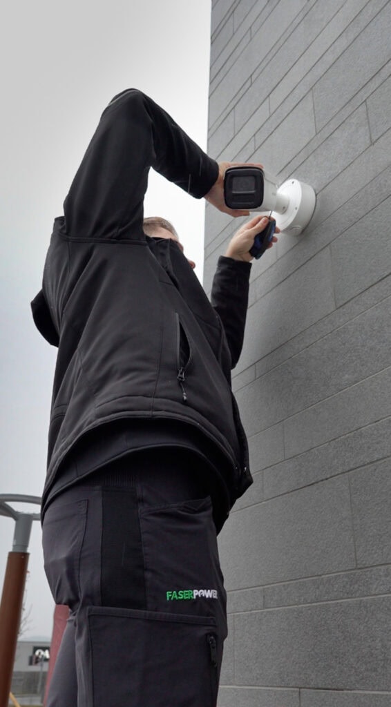 Person installiert Überwachungskamera an grauer Wand für Sicherheit.